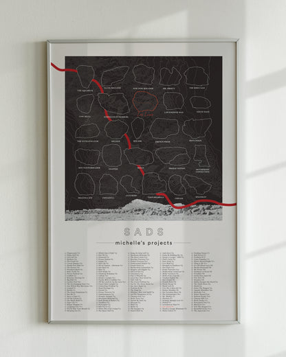 A black color, customized rock climbing ticklist poster for the Sads rock climbing location in Bishop, California. The design has an overlay of crag topography, nature landscapes, and traced boulders, the person's name, and a list of bouldering problems at the bottom. Displayed as wall art in a living room.